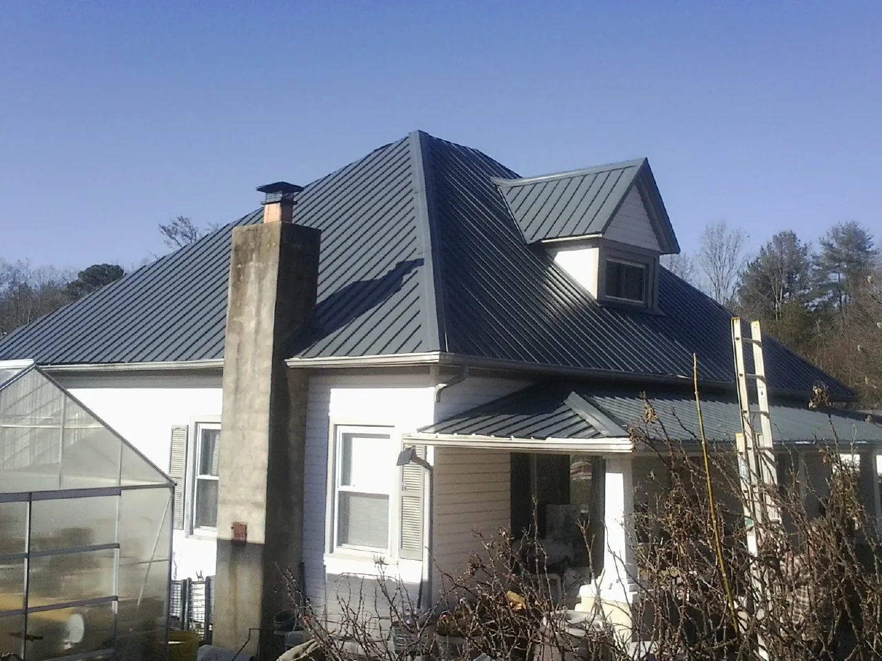 Dark blue standing seam metal roof on a white farmhouse with dormer — Slate & Tile Roof Repair by Roofing Brothers in Walsenburg