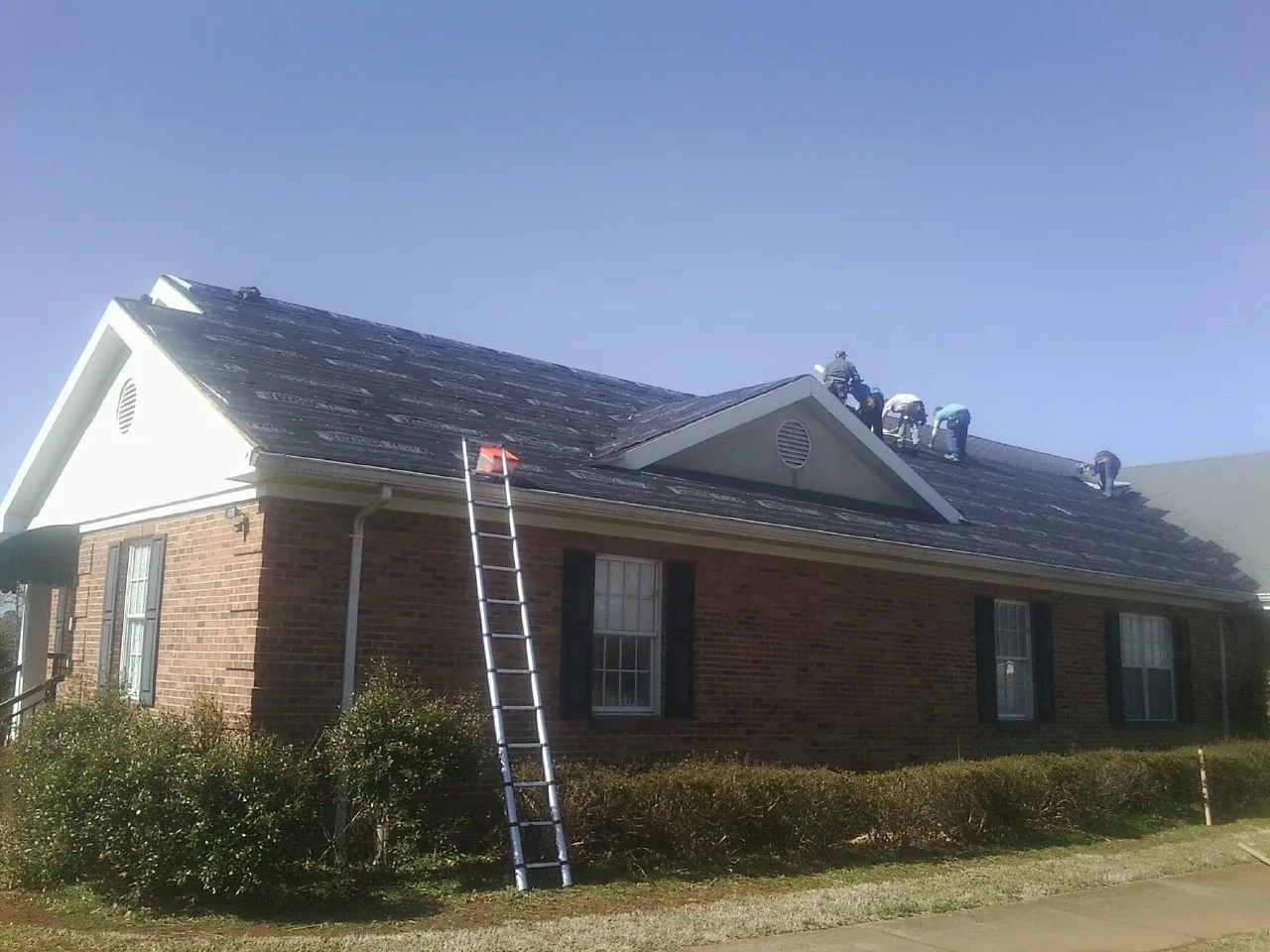 Crew tearing shingles off a brick ranch roof with a ladder set — Metal Roof Repair work by our crew in Walsenburg