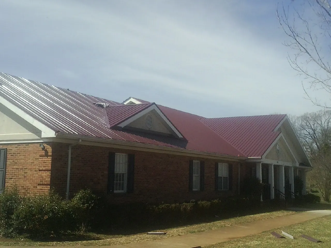 Red metal roof with gabled entries on a long brick building, from a Hail Damage Roof Repair job in Walsenburg