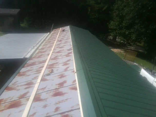 Old rusted panels beside newly installed green metal roofing — Wind Damage Roof Repair by Roofing Brothers in Walsenburg