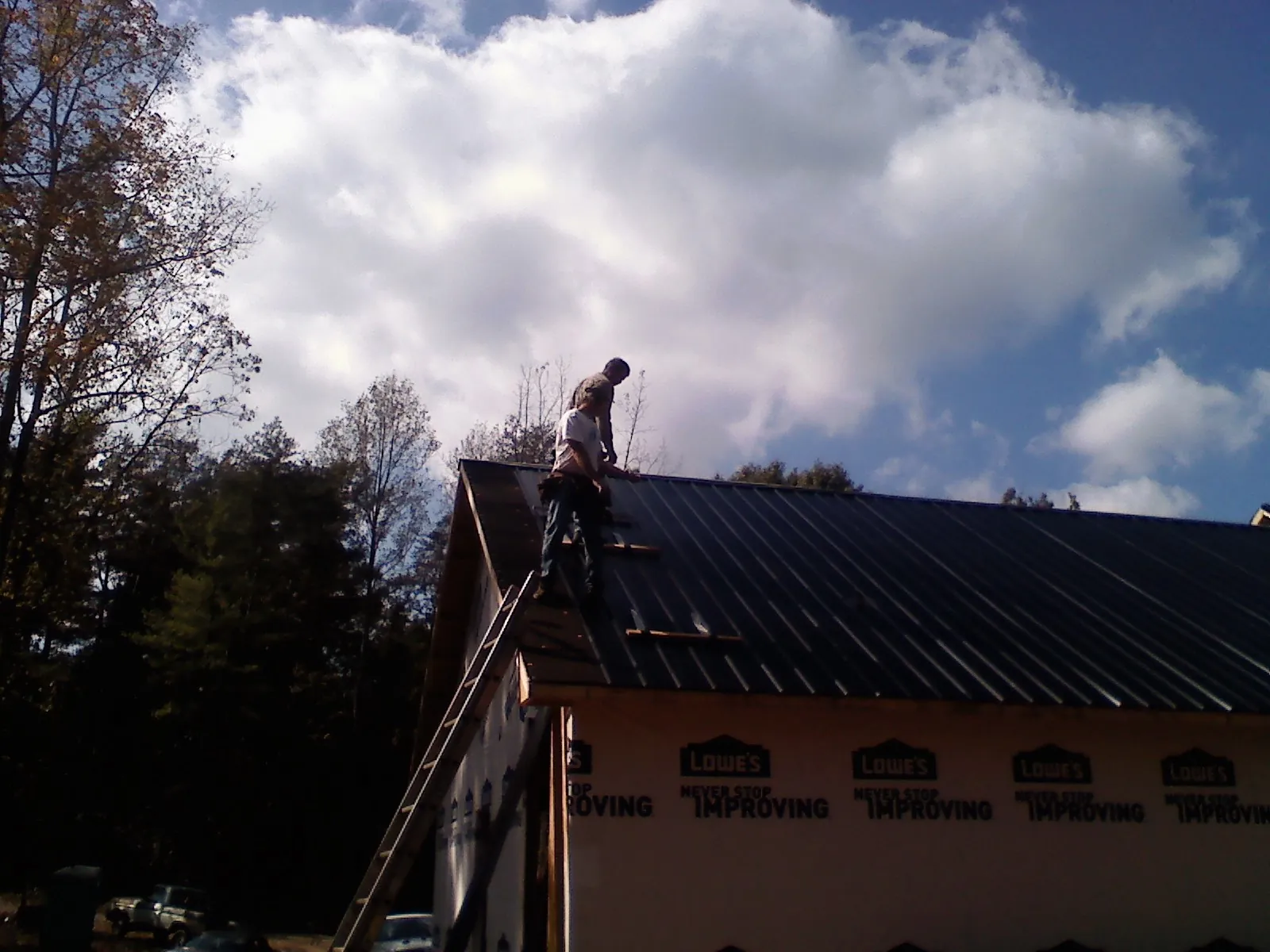 Roofer fastening dark metal panels high against a cloudy sky, from a Roof Inspection job in Walsenburg