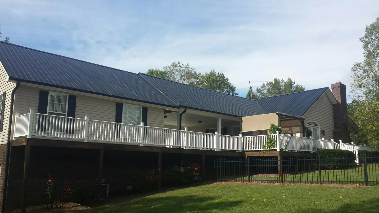 Black metal roof above a long white railed deck on a hillside home in Walsenburg