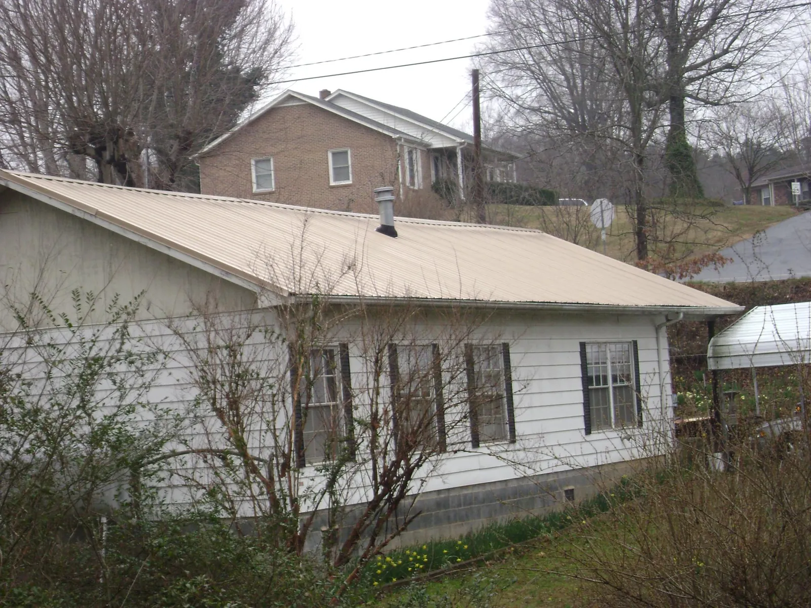 Tan metal roof on a white sided house set into a hillside — Commercial Roofing by Roofing Brothers in Walsenburg